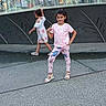 child, girl, posing, walking, fountain, urban, sidewalk, outdoor, playful, smiling, casual_clothing, sandals, daytime, people, background, public_space, building, glass, reflection, street