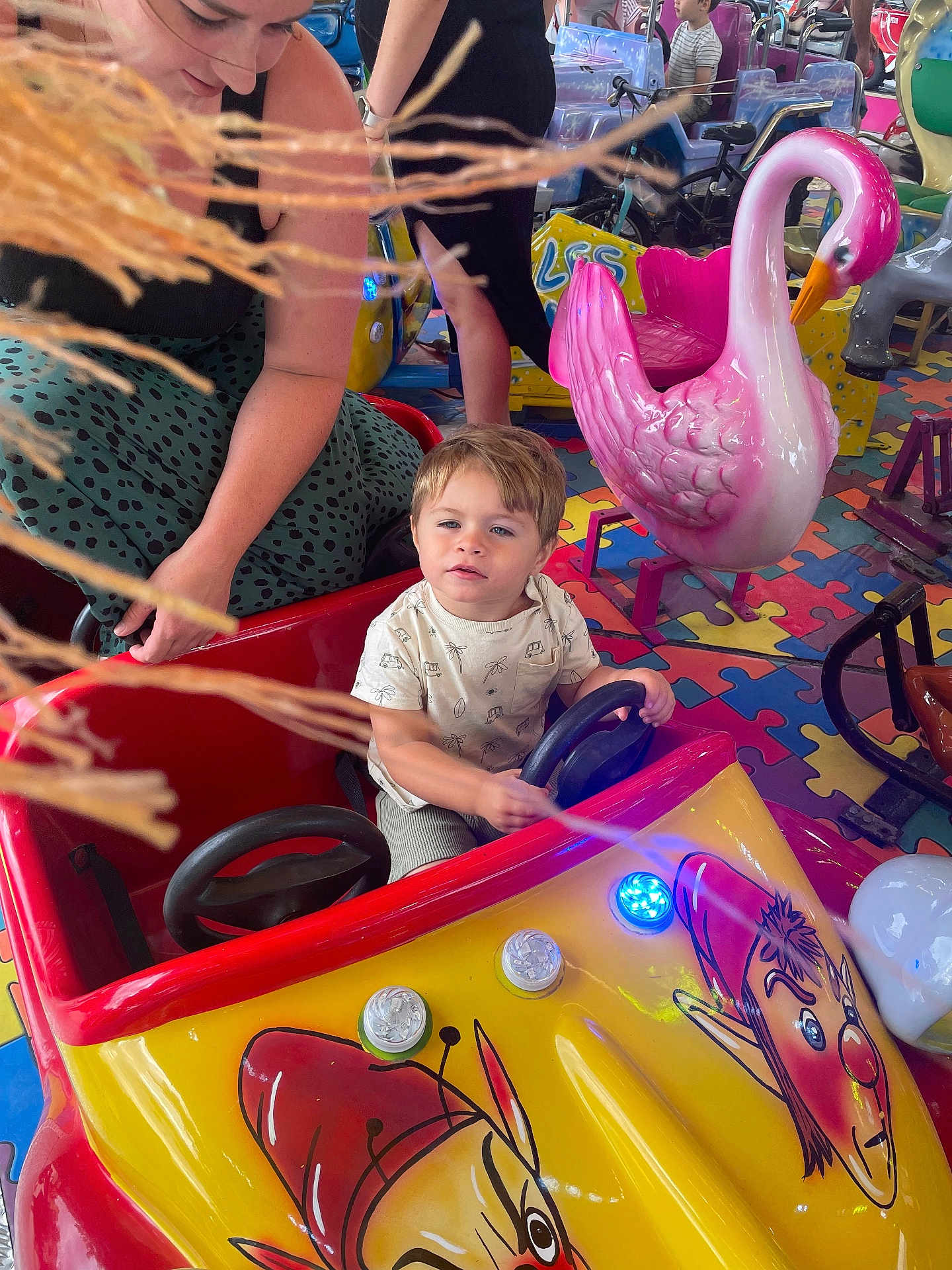 Tiago Jourdain participe au concours pour gagner de l'argent avec cette photo : child, adult, amusement_ride, toy_car, pink_swan, indoor_playground, puzzle_floor, colorful, steering_wheel, person, ride, fun, play, family, woman, curious_expression, seat, entertainment, kid, bright
