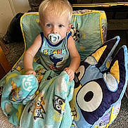 Bentley joined the competition — help win amazing prizes! toddler, child, blanket, pacifier, chair, pillow, cartoon_character, indoor, carpet, fireplace, stone_wall, blue_clothing, cute, home, comfort, young_child, sitting, curious, toy, cozy