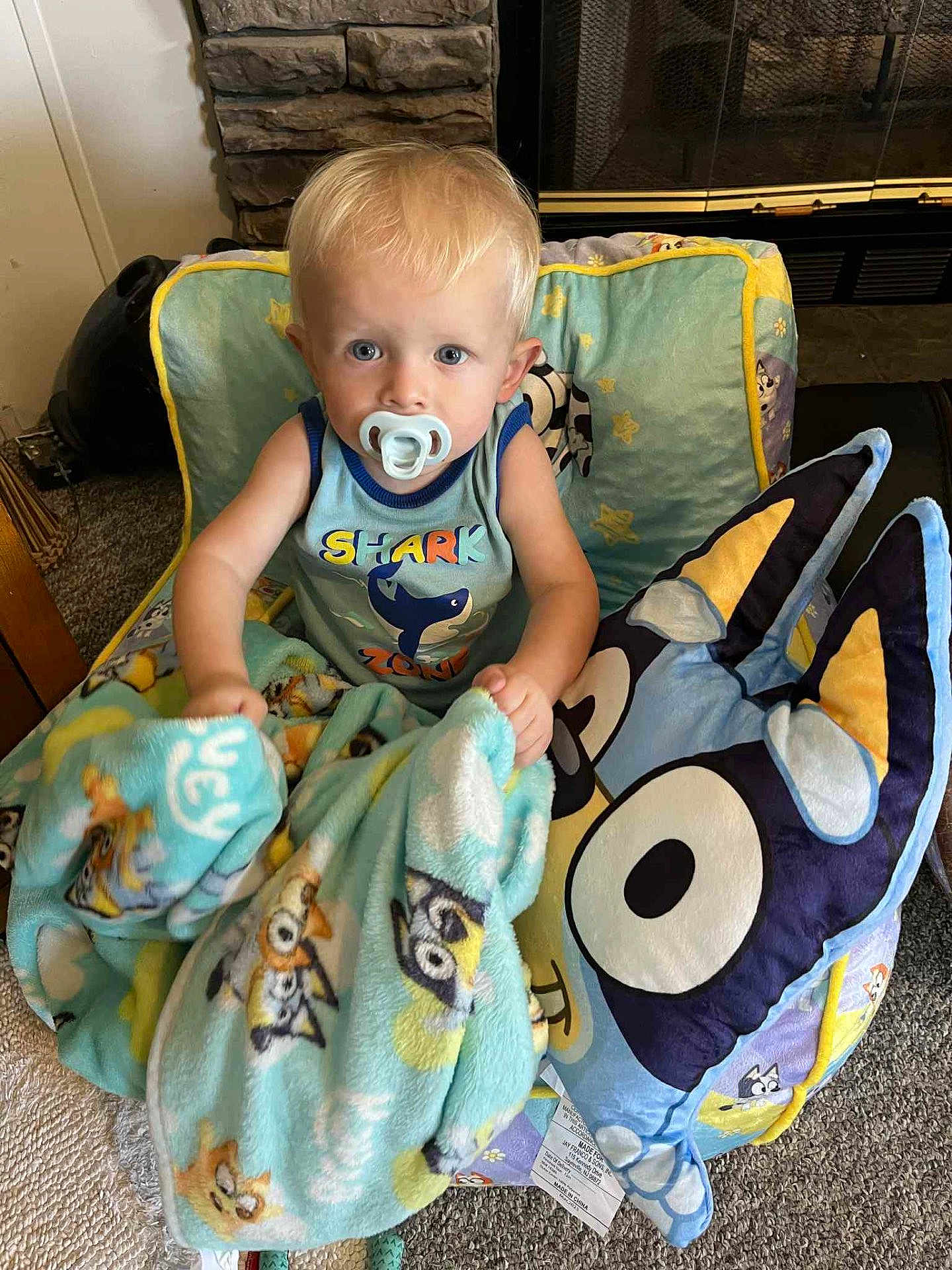 Bentley joined the competition — help win amazing prizes! toddler, child, blanket, pacifier, chair, pillow, cartoon_character, indoor, carpet, fireplace, stone_wall, blue_clothing, cute, home, comfort, young_child, sitting, curious, toy, cozy