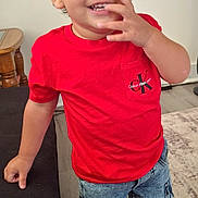 Aurelius is registered to the contest to win money with this photo: toddler, child, curly_hair, red_tshirt, calvin_klein, denim_shorts, sneakers, indoor, couch, wooden_table, smiling, happy, playful, person, floor, carpet, hand, face, standing, casual_clothing