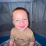 Apolo is registered to the contest to win money with this photo: baby, child, infant, smiling, portrait, indoors, playpen, mesh, seated, brown_shirt, blue_eyes, fair_hair, flash_photography, bedding, patterned_blanket, nursery, happy, cute, closeup, home