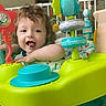 Enzo is registered to the contest to win money with this photo: toddler, child, toy, activity_center, indoor, playtime, colorful, smiling, happy, curly_hair, baby, plastic_toy, floor, cushion, wall_stickers, owl, tree, room, furniture, playful