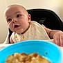 animal_print, baby, bib, blue_bowl, child, closeup, curious, cute, eating, face, feeding_time, focus, food, hand, high_chair, indoor, infant, messy, table, young