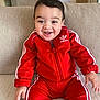 baby, child, smiling, red_tracksuit, adidas, sitting, couch, indoor, happy, face, young_child, clothing, portrait, cute, infant, person, sleeves, hands, jacket, pants