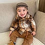 toddler, child, smile, plaid_shirt, brown_pants, boots, cap, couch, indoors, happy, seated, cozy, fashion, portrait, cute, baby, clothing, face, person, home