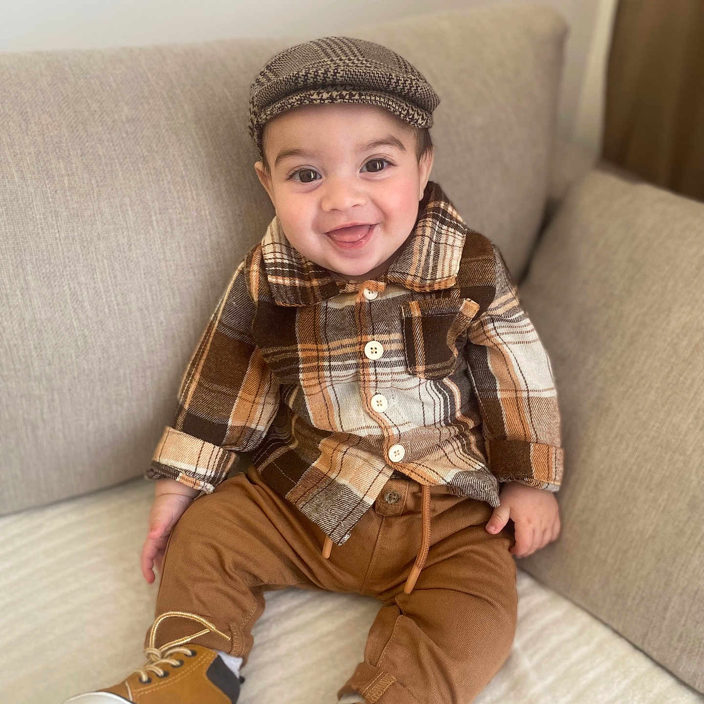 Jayden Winstersheim a rejoint le concours — aidez-le/la à gagner de superbes lots ! baby, boots, brown_pants, cap, child, clothing, couch, cozy, cute, face, fashion, happy, home, indoors, person, plaid_shirt, portrait, seated, smile, toddler