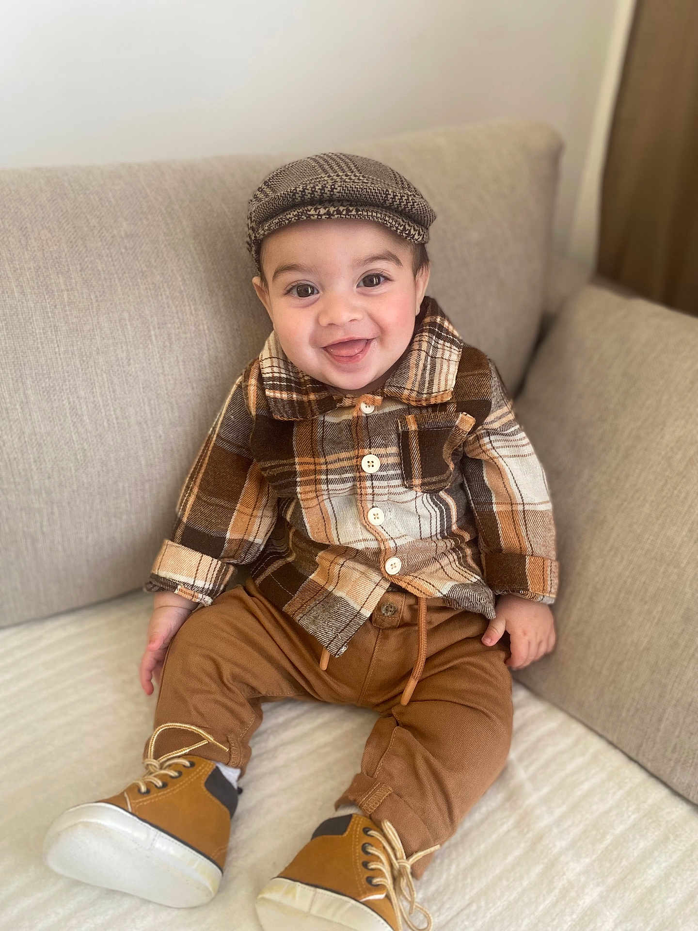 Jayden Winstersheim a rejoint le concours — aidez-le/la à gagner de superbes lots ! toddler, child, smile, plaid_shirt, brown_pants, boots, cap, couch, indoors, happy, seated, cozy, fashion, portrait, cute, baby, clothing, face, person, home