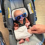 baby, car_seat, sunglasses, infant, hand, floor, footwear, white_cloth, casual, indoor, child, seatbelt, headrest, plastic, safety, tiny_feet, orange_clothing, relaxed, cute, portrait