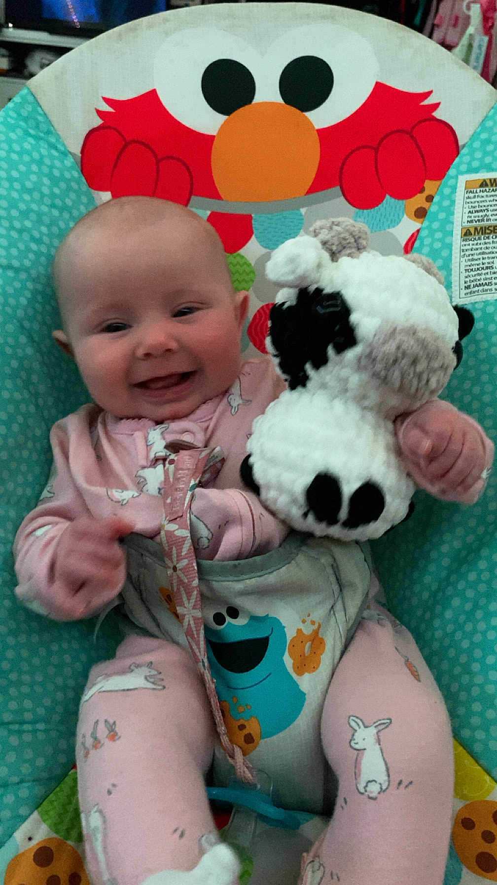 Jade is registered to the contest to win money with this photo: baby, infant, smiling, pajamas, toy, stuffed_animal, bunny_print, baby_seat, elmo, colorful, cute, happy, child, indoor, playful, soft_toy, seat, face, person, clothing