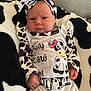 baby, infant, cow_print, headband, blanket, clothing, cute, face, person, portrait, lying_down, animal_print, black_and_white, hand, expression, indoors, soft_texture, child, fashion, newborn