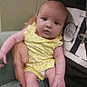 Kayleigh is registered to the contest to win money with this photo: baby, infant, yellow_outfit, polka_dot, adult_hand, calvin_klein, black_shirt, curious_expression, indoor, couch, person, holding, portrait, cute, child, soft_lighting, closeup, skin, face, small