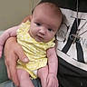 baby, infant, yellow_clothing, polka_dot, adult_hand, calvin_klein, tshirt, chain, jewelry, face, skin, person, holding, casual_clothing, jeans, seated, indoor, portrait, cute, curious