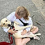 Harper is registered to the contest to win money with this photo: affection, animal, blonde_hair, casual_clothing, concrete, crocs, dog, footwear, harness, holding, leash, outdoor, pavement, person, pet, relaxed, sidewalk, sitting, water