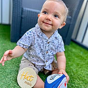 Marius participe au concours pour gagner de l'argent avec cette photo : baby, background, child, face, foot, grass, green, hand, happy, month_marker, outdoor, patterned_clothing, rugby_ball, shirt, shorts, sitting, smile, toy, wicker_chair, wooden_sign