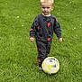 toddler, child, soccer_ball, grass, outdoor, greenery, clothing, mickey_mouse, playful, sports, young_child, standing, casual_wear, footwear, toy, game, nature, portrait, daylight, activity