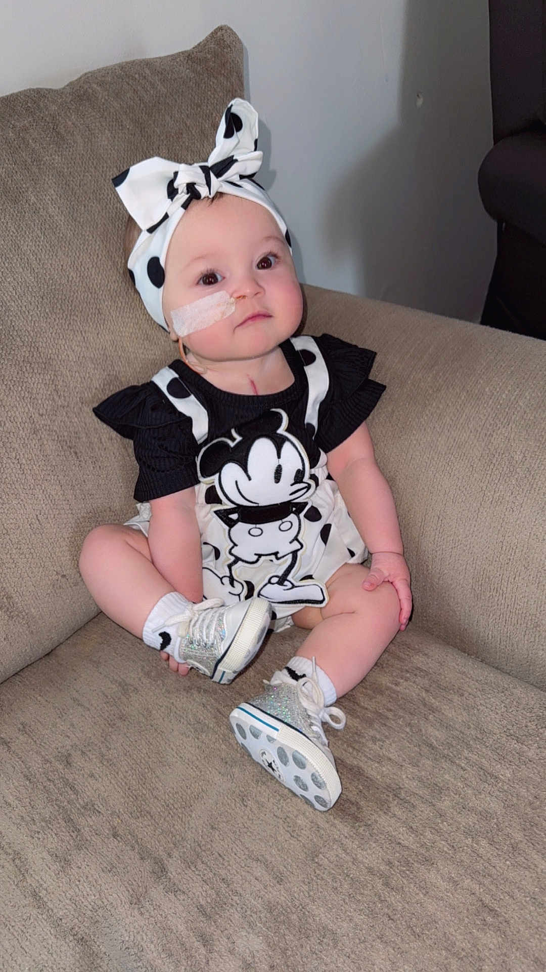 Ariella joined the competition — help win amazing prizes! baby, child, infant, headband, mickey_mouse, clothing, shoes, socks, face, medical_tape, couch, furniture, sitting, indoor, cute, portrait, polka_dot, young_child, person, apparel