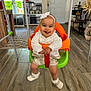 baby, basket, carpet, child, curtains, door, furniture, happy, headband, indoor, plant, shelf, shoes, smiling, swing, table, tongue_out, white_clothing, window, wood_floor