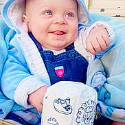 Jordan is registered to the contest to win money with this photo: baby, blue_hoodie, blanket, child, cute, denim_overalls, door, face, hand, indoor, infant, light_blue, person, plush, smiling, soft_toy, tongue_out, toy, young_child, warm_clothing