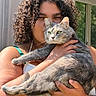 Rocksie Russell is registered to the contest to win money with this photo: cat, person, portrait, curly_hair, smiling, green_eyes, gray_fur, whiskers, pet, holding, arms, outdoor, sunlight, window, indoor, closeup, animal, feline, floral_clothing, bracelet