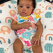 Neorah is registered to the contest to win money with this photo: baby, infant, child, bow, blue_bow, onesie, floral_pattern, socks, cushion, animal_pattern, rainbow_pattern, face, hands, legs, curious, indoor, soft_toys, colorful, lying_down, portrait