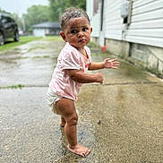 Maizie joined the competition — help win amazing prizes! toddler, child, barefoot, pink_shirt, diaper, wet_ground, concrete, outdoor, puddle, curious, expression, standing, side_view, short_hair, residential, house, driveway, daylight, person, young_child