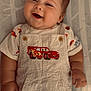 baby, smile, overalls, cartoon_car, blanket, pattern, happy, infant, cute, child, clothing, face, cheeks, lying_down, button, hand, short_sleeve, fabric, portrait, closeup