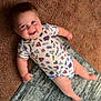 baby, child, smiling, onesie, superhero, carpet, rug, indoor, cute, happy, infant, person, face, skin, hand, foot, clothing, laying, cheerful, portrait