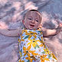 baby, child, infant, smiling, face, arms, dress, floral_pattern, blanket, soft_texture, outdoor, sunlight, shadow, happy, cute, lying_down, green_pants, portrait, young_child, person