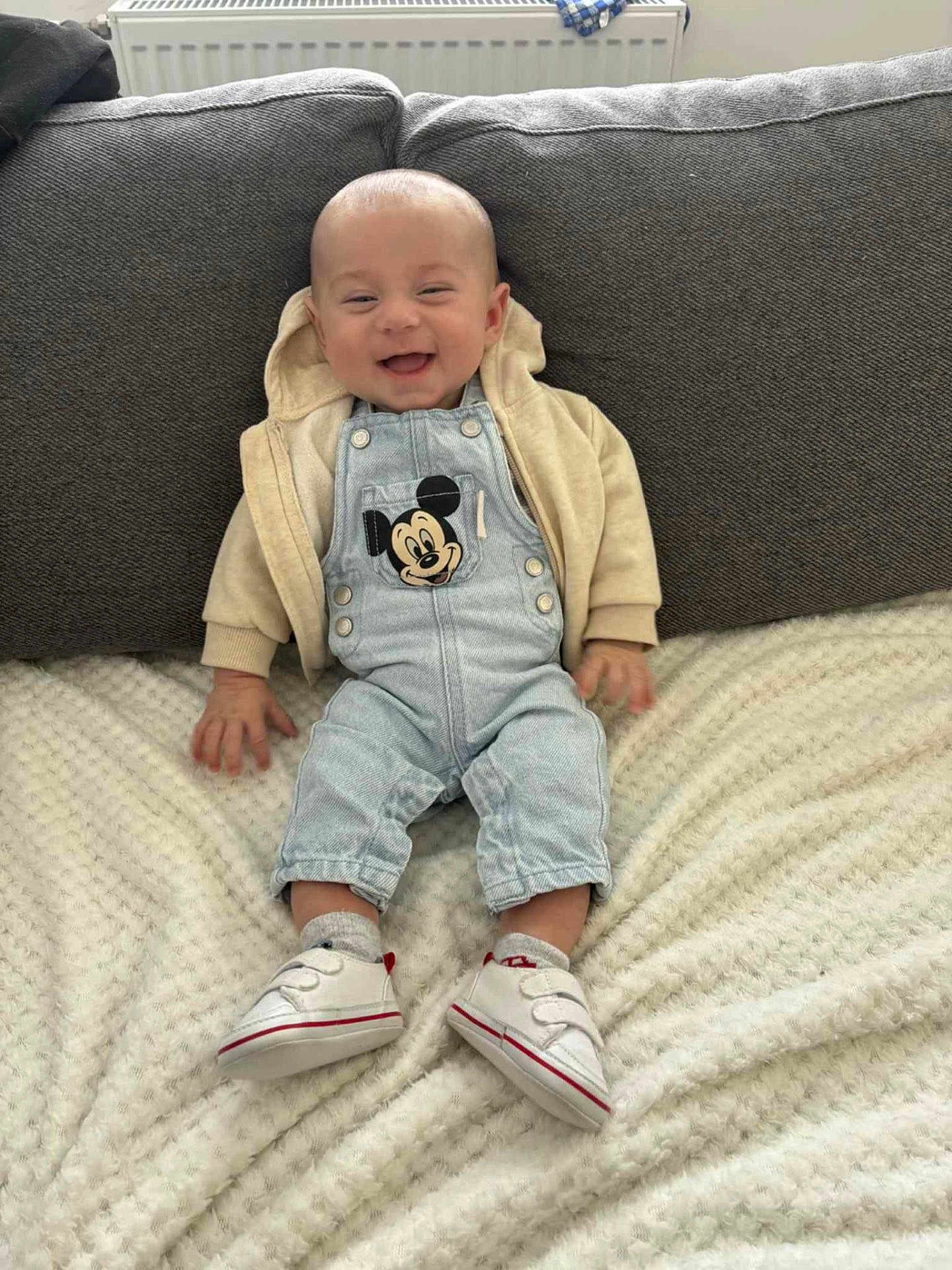 Maëlo participe au concours pour gagner de l'argent avec cette photo : baby, smiling, denim_overalls, mickey_mouse, hoodie, sitting, blanket, white_shoes, socks, couch, happy, infant, cute, clothing, indoor, portrait, child, funny_face, cozy, comfortable