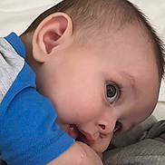 William is registered to the contest to win money with this photo: baby, infant, face, closeup, child, blue_clothing, skin, head, eyes, mouth, hand, sleeping_area, soft_light, portrait, cute, toddler, human, young_child, expression, laying_down
