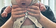 William is registered to the contest to win money with this photo: baby, child, adult, hands, clothing, shirt, pants, face, expression, surprised, indoor, window, light, person, holding, portrait, cute, young, human, background