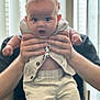 William is registered to the contest to win money with this photo: baby, child, adult, hands, clothing, shirt, pants, face, expression, surprised, indoor, window, light, person, holding, portrait, cute, young, human, background
