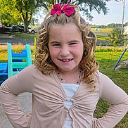 Harper is registered to the contest to win money with this photo: child, girl, blonde_hair, curly_hair, pink_bow, smile, outdoor, playground, grass, tree, necklace, casual_clothing, confident, happy, daylight, park, young, person, nature, portrait
