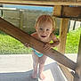 child, toddler, smiling, barefoot, wood, outdoor, sunlight, playful, diaper, greenery, fence, patio, beam, shadow, happy, person, summer, daylight, nature, cute