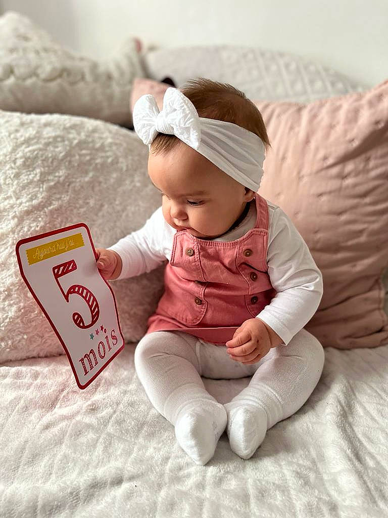 Leia participe au concours pour gagner de l'argent avec cette photo : baby, baby_toddler_clothing, baseball_cap, cap, carmine, child, comfort, finger, flooring, happy, linens, person, product, room, sitting, sleeve, smile, t_shirt, toddler, vertebrate