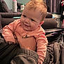 Jaime is registered to the contest to win money with this photo: adult_hand, baby, child, clothing, couch, curtain, drink_can, face, furniture, hair, hand, happy, indoor, jacket, living_room, person, pink, sleeve, smiling, window