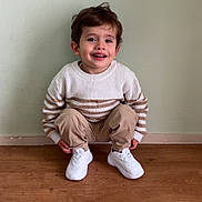 Noham participe au concours pour gagner de l'argent avec cette photo : child, smiling, indoor, sweater, striped_clothing, pants, white_sneakers, floor, wooden_floor, wall, light_green_wall, happy, portrait, casual_clothing, young_child, sitting_pose, person, cute, cozy, candid