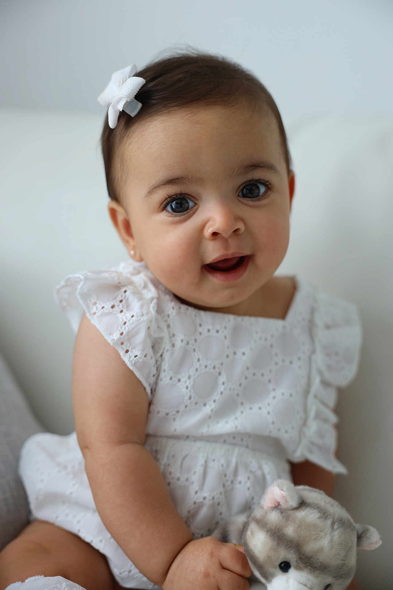 Miana is registered to the contest to win money with this photo: baby, child, infant, girl, white_dress, bow, plush_toy, stuffed_animal, cute, smiling, portrait, indoors, soft_toy, happy, sitting, closeup, eyelashes, skin, arm, face