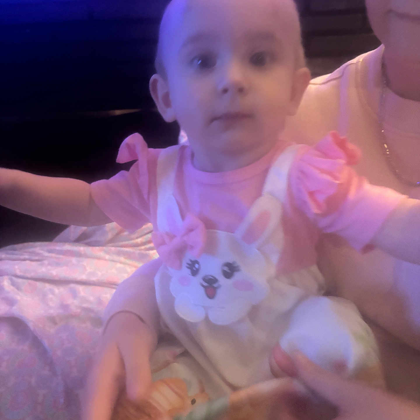 Luna is registered to the contest to win money with this photo: baby, child, person, pink_clothing, bunny_design, adult_hand, glasses, indoor, fabric, holding, face, portrait, cute, infant, sitting, soft_lighting, blurred, purple_hue, short_hair, young_child