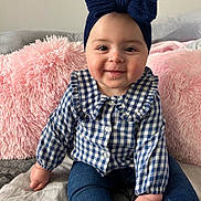 Ornella a rejoint le concours — aidez-le/la à gagner de superbes lots ! baby, bed, blue_clothing, bow, checkered_shirt, child, cozy, cute, face, fluffy, hand, headband, indoor, jeans, person, pillow, pink, portrait, sitting, smiling