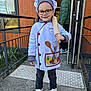 Isaac a rejoint le concours — aidez-le/la à gagner de superbes lots ! child, chef_costume, rolling_pin, glasses, smiling, outdoor, concrete, doorway, person, jacket, sneakers, apron, hat, cartoon, building, window, railing, plants, concrete_path, happy