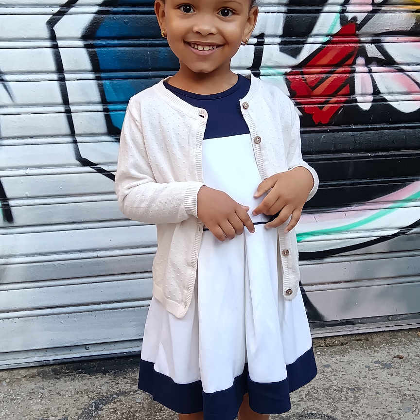 Aurore a rejoint le concours — aidez-le/la à gagner de superbes lots ! cardigan, casual, child, colorful, concrete, dress, earrings, fashion, girl, graffiti, happy, outdoor, person, portrait, sandals, smiling, standing, street, urban, young
