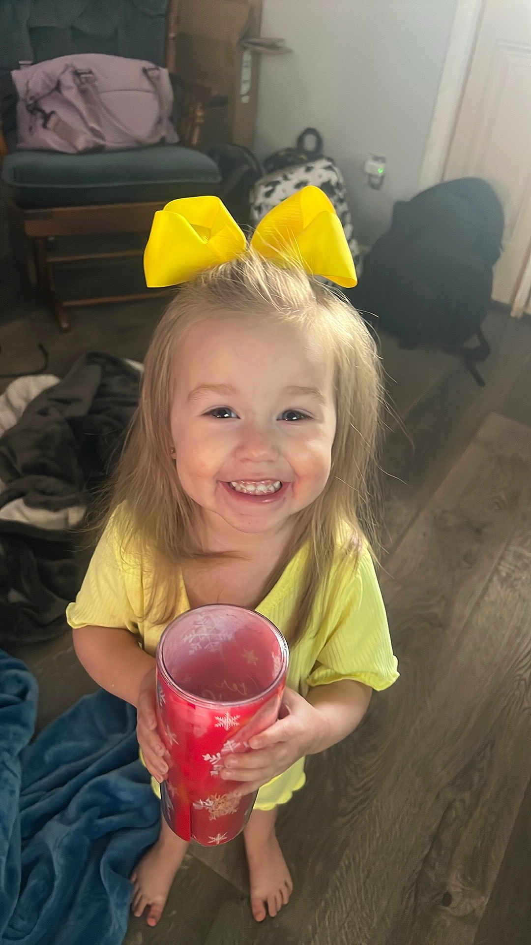 Braeleigh joined the competition — help win amazing prizes! child, girl, yellow_bow, smiling, happy, barefoot, red_cup, snowflake_pattern, yellow_dress, wooden_floor, blanket, indoor, bag, backpack, cheerful, portrait, cute, holding_object, home, small_person