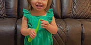 Braeleigh is registered to the contest to win money with this photo: toddler, child, smiling, green_outfit, pink_bow, toy, indoor, leather_couch, flooring, sandals, happy, person, small_child, cute, playful, home, portrait, standing, face, furniture