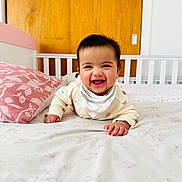 Anabia is registered to the contest to win money with this photo: baby, smiling, bed, pillow, crib, wooden_door, indoors, child, happy, face, clothing, blanket, nursery, person, infant, cute, toddler, sleepwear, lying_down, home