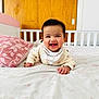 baby, smiling, bed, pillow, crib, wooden_door, indoors, child, happy, face, clothing, blanket, nursery, person, infant, cute, toddler, sleepwear, lying_down, home