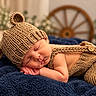 newborn, baby, sleeping, infant, portrait, knitted_hat, knitted_clothing, brown, navy_blanket, cozy, peaceful, indoors, bed, blanket, closeup, resting, face, hands, soft_lighting, photography