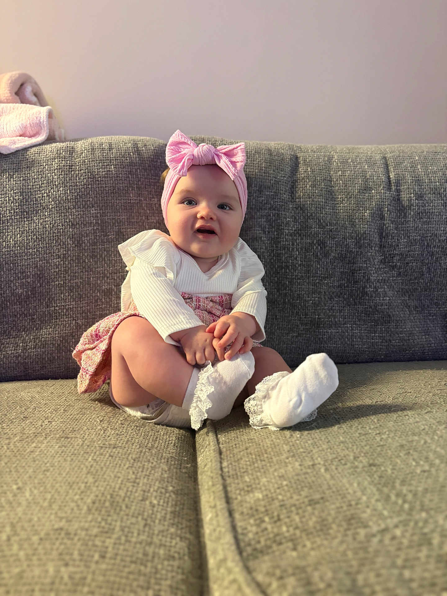 Willow joined the competition — help win amazing prizes! baby, child, infant, girl, headband, bow, white_clothing, pink_clothing, socks, lace, couch, sofa, furniture, indoor, portrait, cute, smiling, hands, seated, cozy
