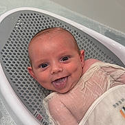 Theo is registered to the contest to win money with this photo: baby, baby_bath_seat, bath, bathtub, child, closeup, cute, face, happy, head, indoors, infant, person, playful, skin, smiling, tongue_out, towel, water, wet
